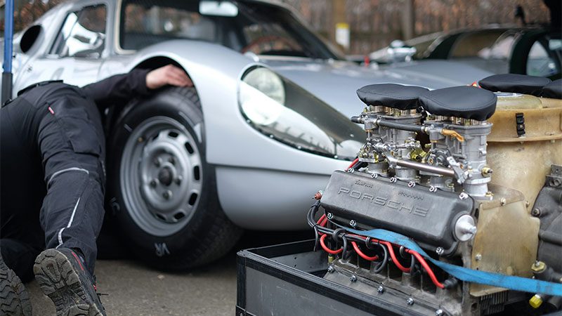 A mechanic working on an old Porsche vehicle with an exposed Porsche cars engine