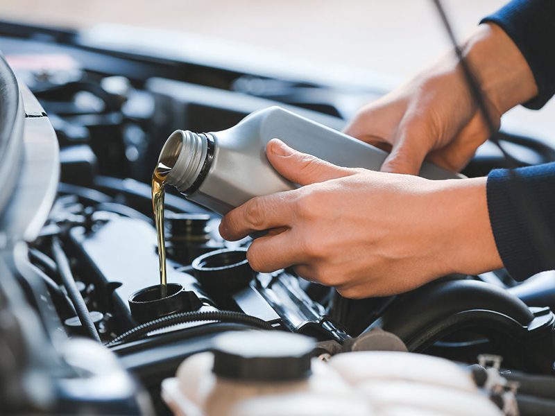 Male mechanic refilling engine oil under the hood of a car at an auto service center, performing routine maintenance.