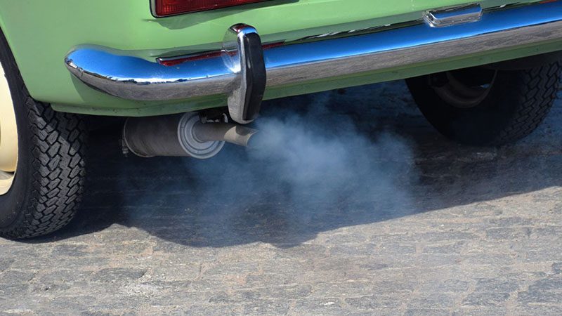Blue exhaust fumes coming from the tailpipe of an old car, indicating possible engine or oil-burning issues.