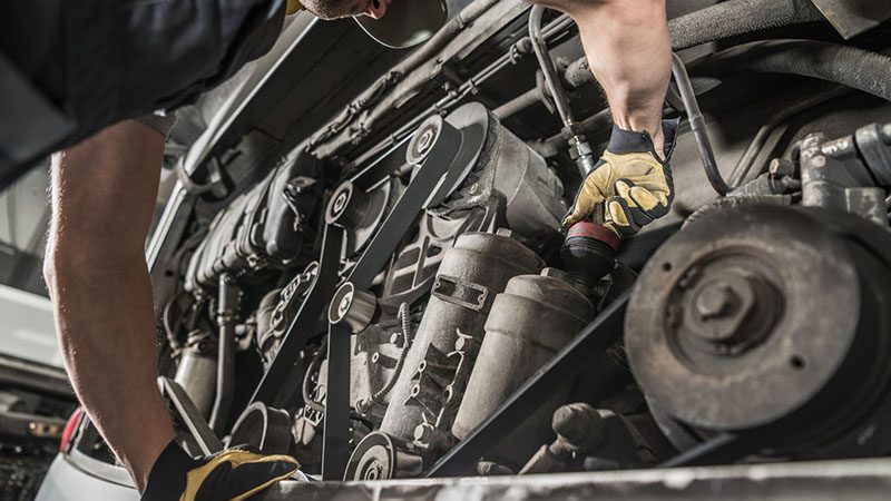 Auto mechanic repairing a car engine in a workshop, focusing on engine components and diagnostics.