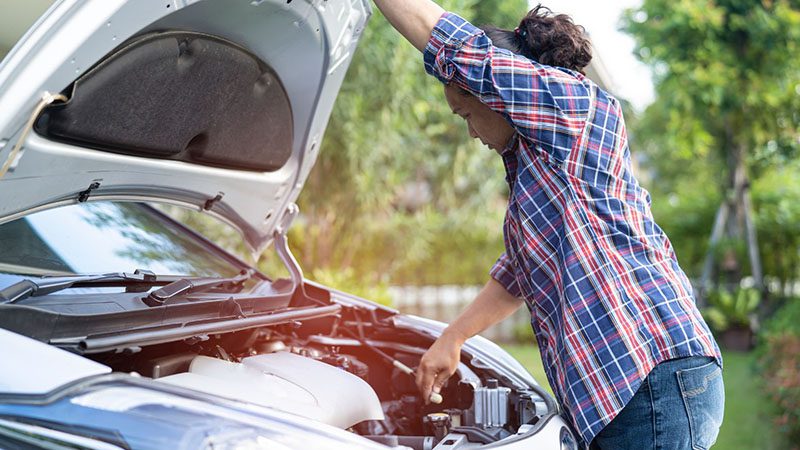 Mechanic inspecting and repairing a car engine under the open hood.
