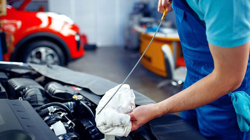 Auto service worker checking the engine oil level using a dipstick during routine car maintenance.