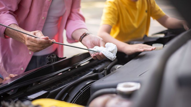 Man checking the oil level of a car engine using a dipstick during routine maintenance.
