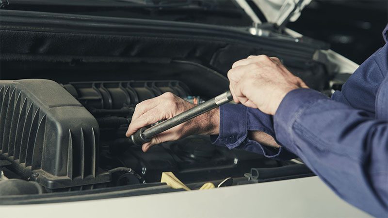 Mechanic manually performing a car engine tune-up using hand tools in a workshop.