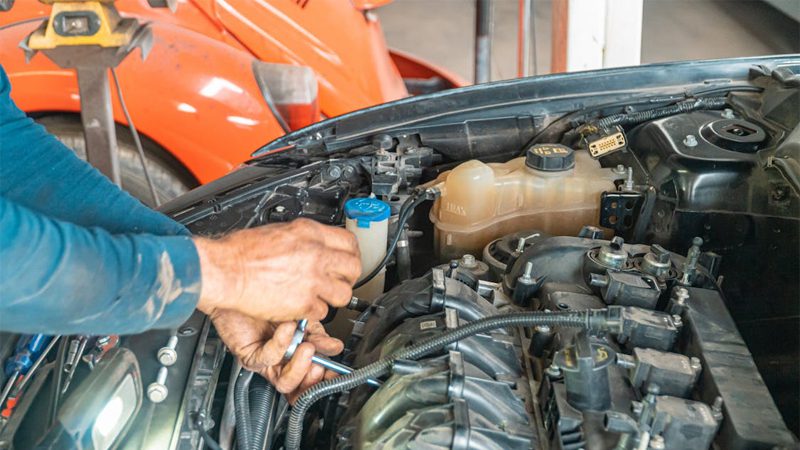 Mechanic performing a tune-up on an old car engine during maintenance in a workshop.