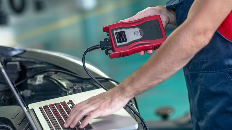 Mechanic using laptop to conduct car diagnostics, identifying causes of limp mode through ECU fault codes.