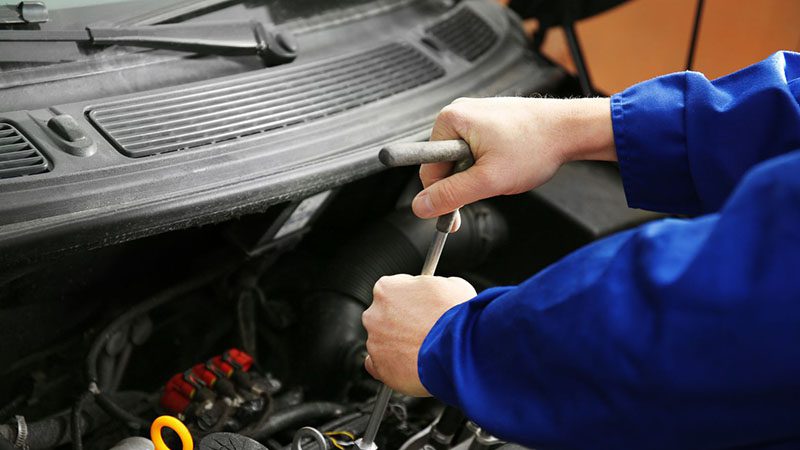 Mechanic repairing a car with the hood open during engine maintenance at an auto service shop.