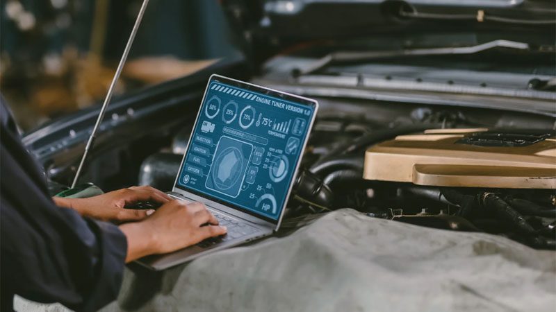 Mechanic in a garage using a laptop to check car engine combustion control or ECU diagnostics.