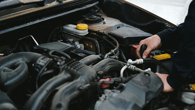 Man performing a visual inspection of a car engine under the hood.