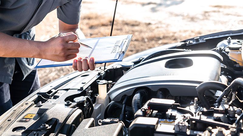 Technician performing engine repair checklist and writing on clipboard during car service.