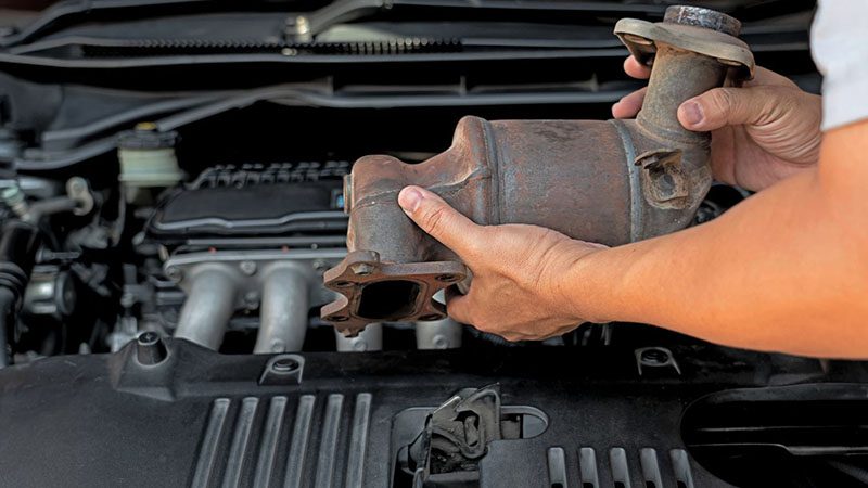 Technician holding a clogged old catalytic converter removed from a gasoline car engine.