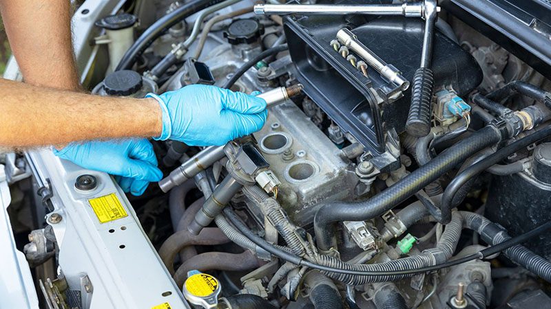Replacing a misfiring spark plug during car engine repair.