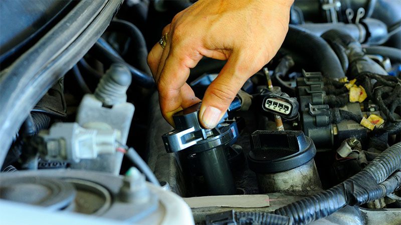 Mechanic installing a coil pack into a car engine for proper ignition function.