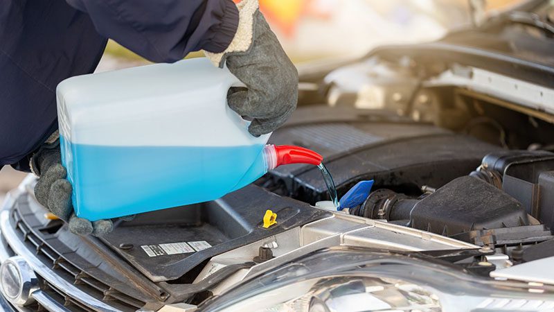 Mechanic adding antifreeze coolant to car engine radiator for temperature regulation