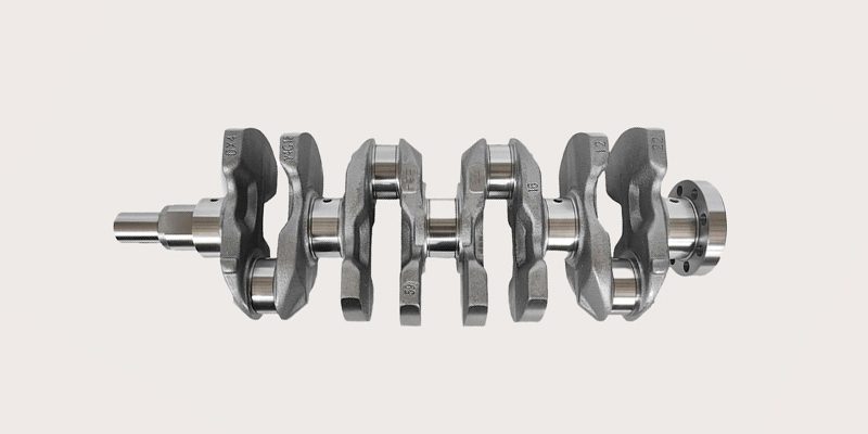 Close-up view of a car engine crankshaft, highlighting the main journals, counterweights, and fine machining details.