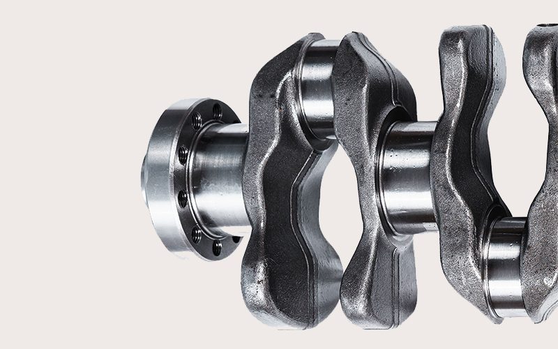 Close-up view of a crankshaft, highlighting the detailed machining of the journals, counterweights, and flange.