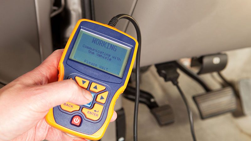 Hand holding an OBDII scanner connected to a vehicle to diagnose engine issues and read error codes