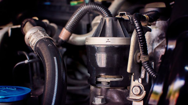 Close-up of an old Exhaust Gas Recirculation (EGR) valve in the engine compartment, used to reduce carbon monoxide emissions.