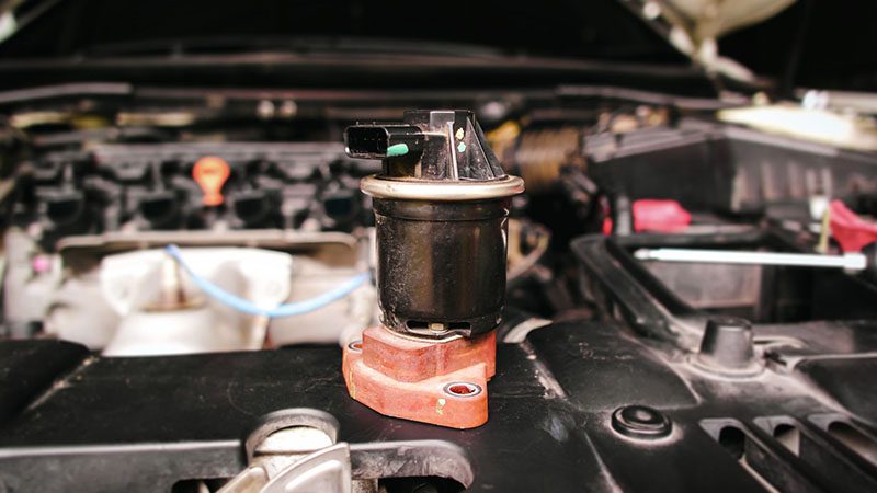 Close-up of a damaged EGR (Exhaust Gas Recirculation) valve in the engine compartment, highlighting a worn automotive emission component.