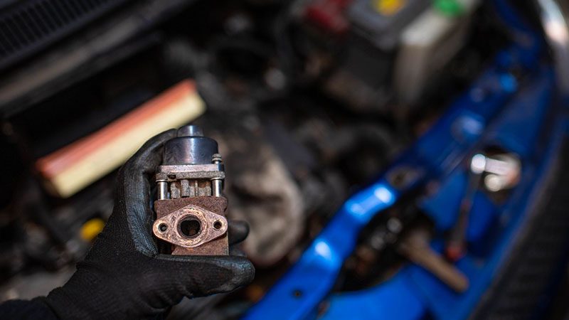 Contaminated EGR valve from a car engine showing carbon buildup and soot deposits.