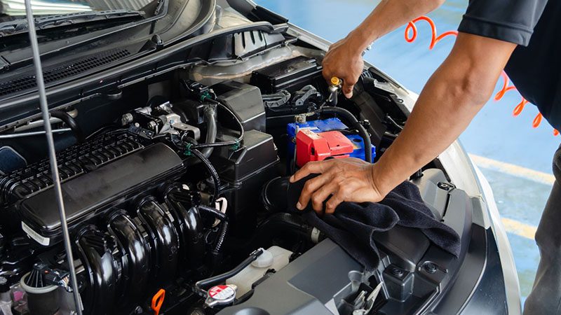 Mechanic cleaning a car engine with a cloth during maintenance.