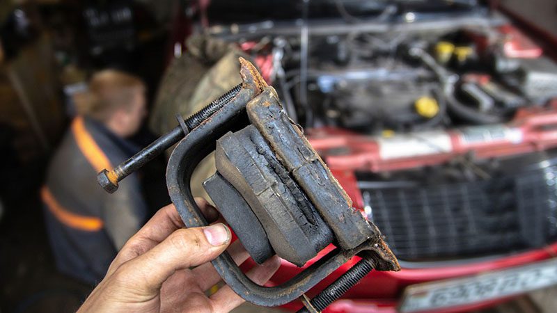 Torn and faulty engine mount placed on the garage floor during inspection.