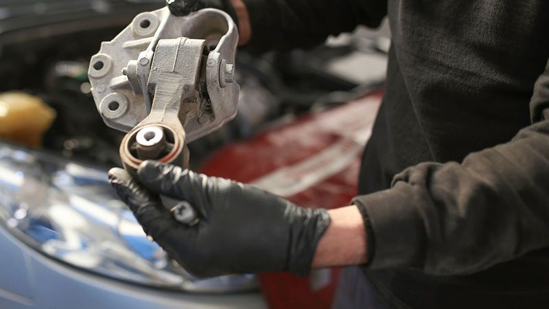 Mechanic performing engine mount replacement under the vehicle hood.