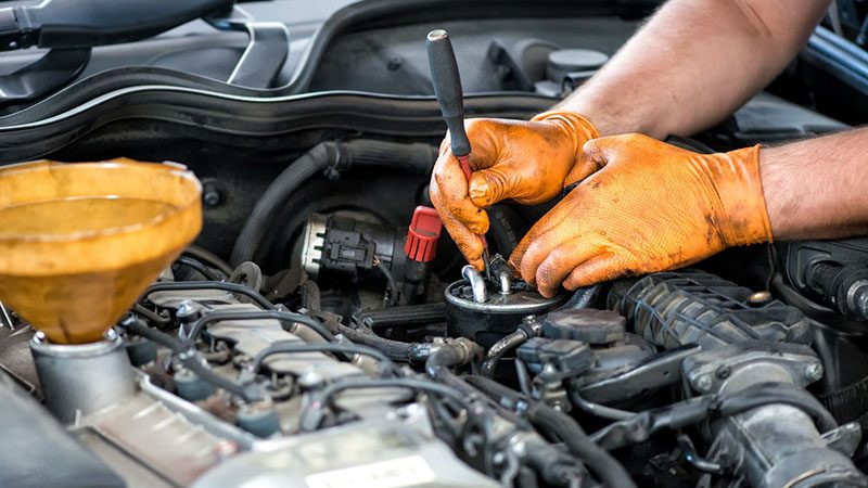 Mechanic working on a diesel fuel filter, performing maintenance to prevent engine performance and power loss issues.