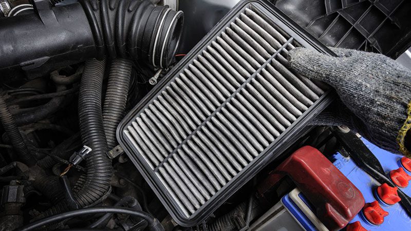 Technician changing a car air filter to improve airflow and prevent reduced engine power issues.