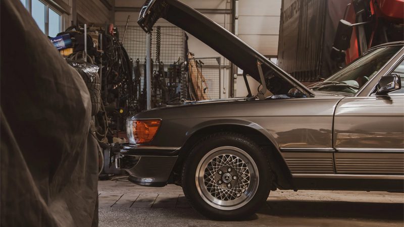 Grey car parked in a garage with hood lifted, prepared for engine inspection or diagnosis of reduced power issue.