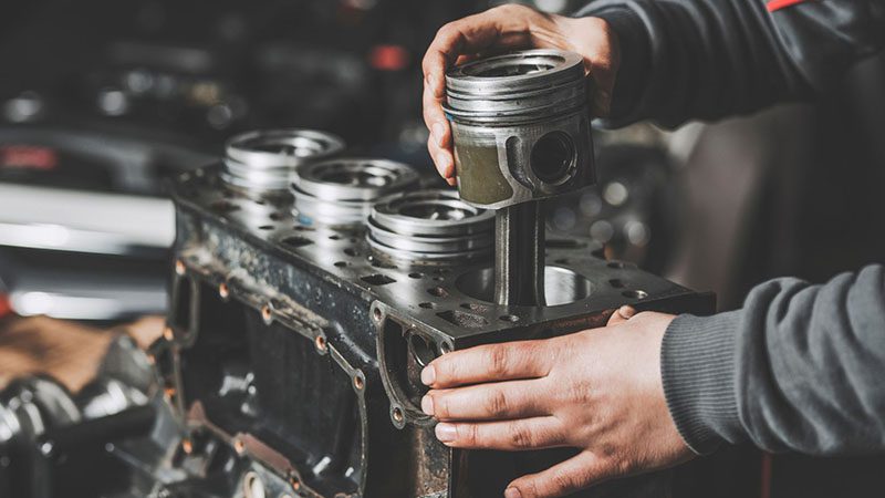 Mechanic installing pistons into an engine, demonstrating key internal components related to engine specifications.