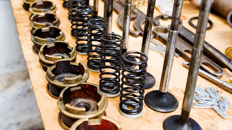 Close-up of engine valve components including the valve head, stem, spring, and seat, arranged on a workbench for inspection or assembly.
