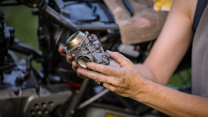 Close-up of mechanic hands holding a carburetor during engine maintenance.