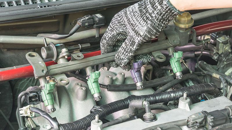 Car mechanic inspecting the fuel injector system during vehicle maintenance.