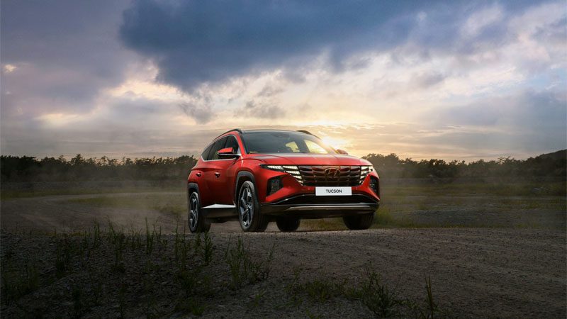 Red Hyundai Tucson driving on the road, showcasing modern SUV design and performance