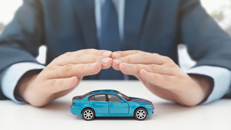 Car insurance concept with vehicle model under protective hands symbolizing safety and coverage
