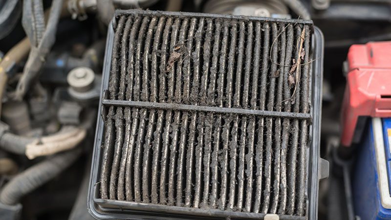 Close-up of a dirty car engine air filter showing accumulated dust and debris.