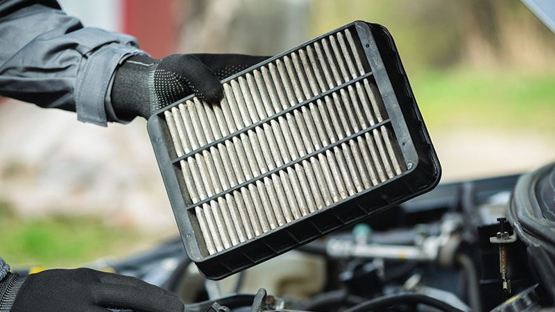 Car service worker holding an old car engine air filter in hands.
