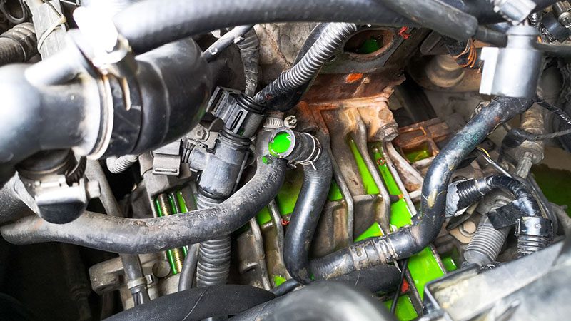 Green coolant leaking from a car radiator, indicating a cooling system problem.