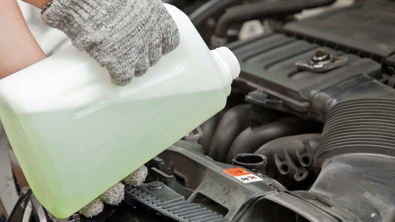 Mechanic pouring coolant into a car’s reservoir under the hood.