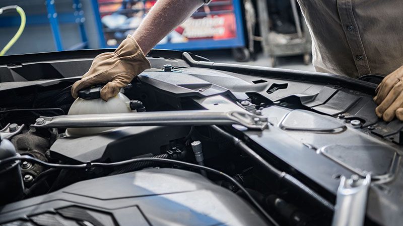 Car mechanic checking engine coolant level in the reservoir under the hood.