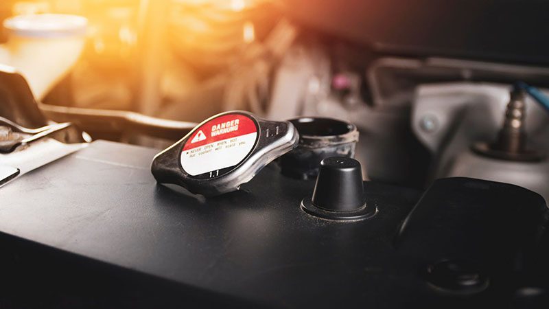 Radiator cap marked 1.1 bar opened and placed on the car radiator.