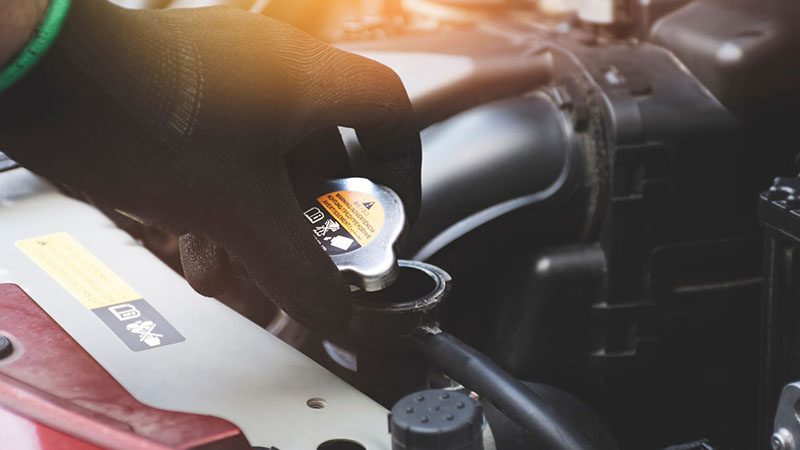 Mechanic’s hand opening a car radiator cap to check coolant level.