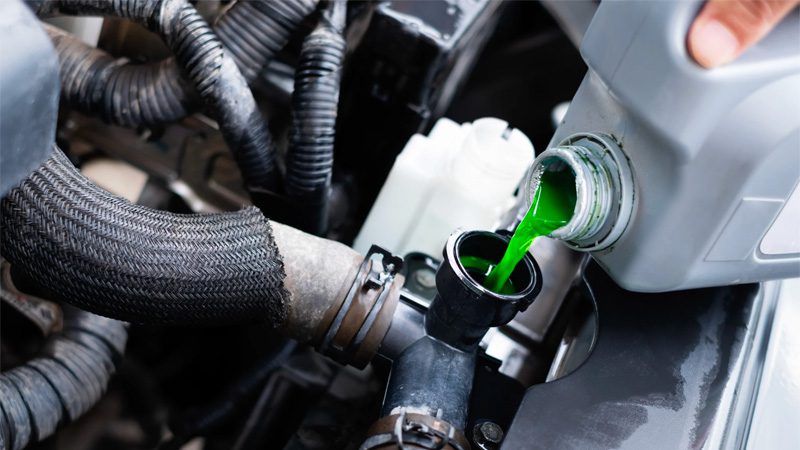 Pouring coolant into a car’s reservoir under the hood.