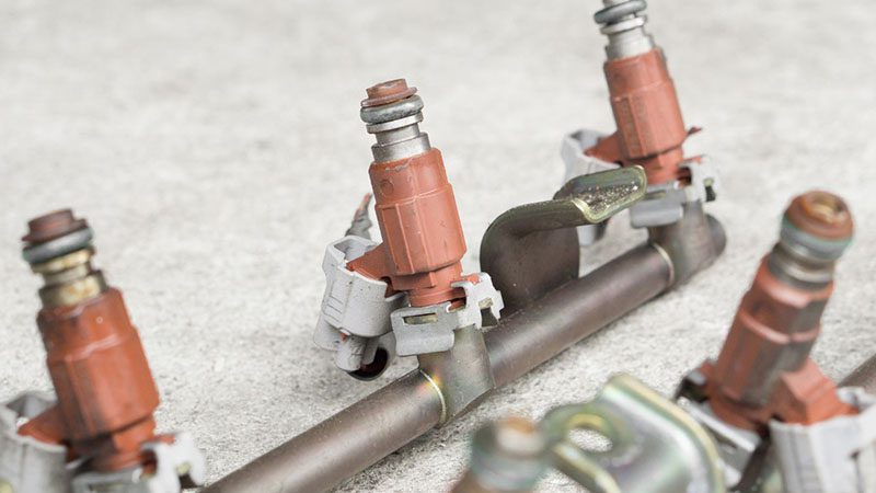Old and used fuel injectors with injector rail for a gasoline engine, placed on a workshop table
