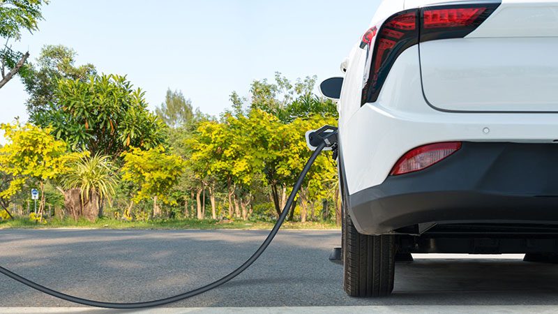 Hybrid car plugged into a charging station on the side of the road, emphasizing eco-friendly driving.