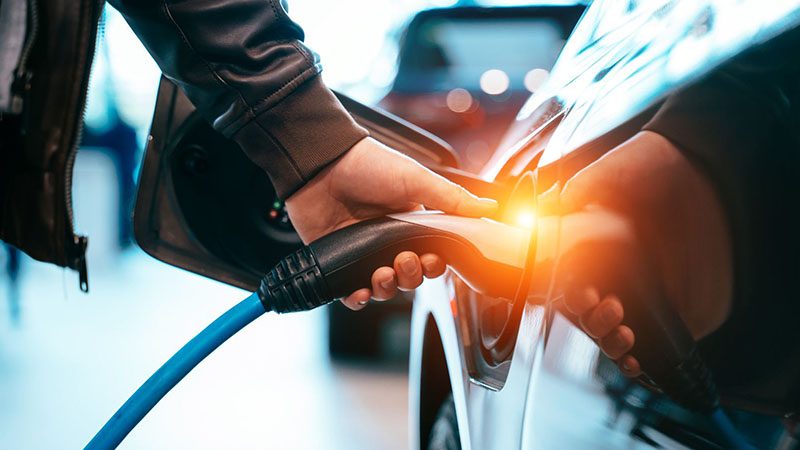 A man holding a charging cable and plugging it into the port of a hybrid car, demonstrating the charging process.