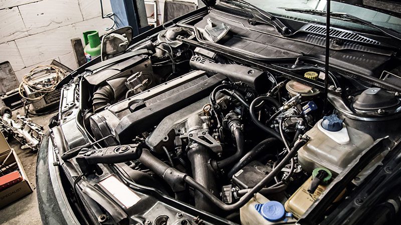 Close-up of a car hood lifted up, revealing the engine compartment and mechanical components.