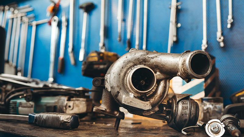 Turbo engine placed on a repair desk in a mechanic workshop, surrounded by tools and engine parts.