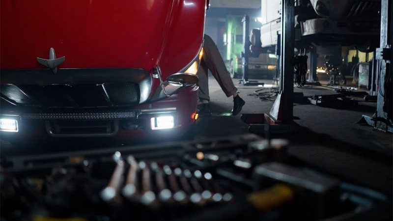 Mechanic working on a truck in a dimly lit garage, focused on repair and maintenance.